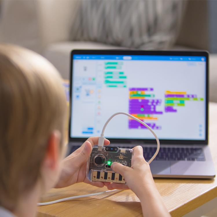 Los kits STEM de suscripción Nextmaker Box de Makeblock, ilustrados por un niño que sostiene una pieza de electrónica programable frente a una computadora portátil que muestra su código basado en bloques