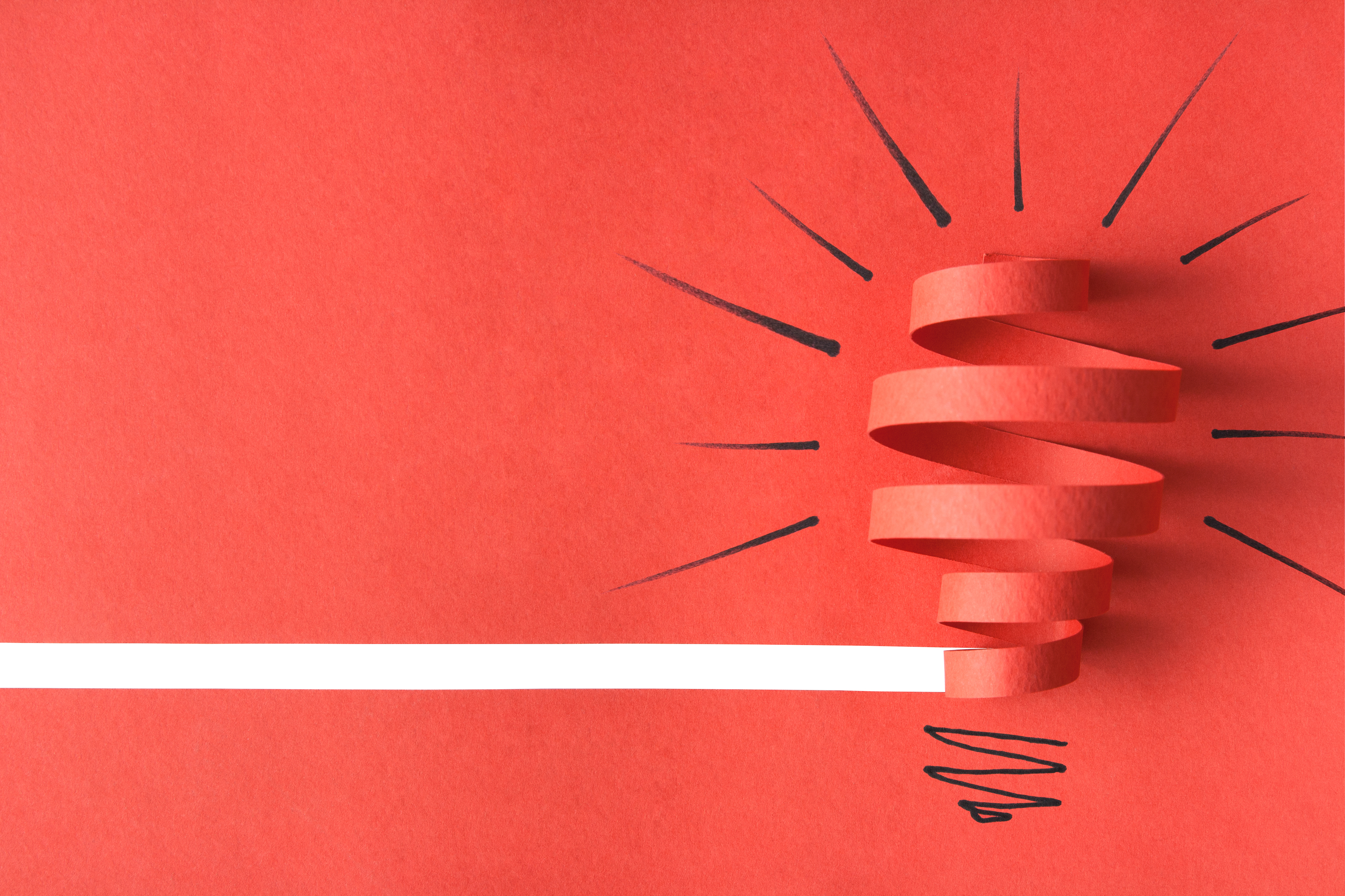 Image of a light bulb cut from red paper on a red background.