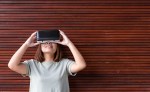 Young asian woman with virtual reality simulator while standing in living room and wood material wall background