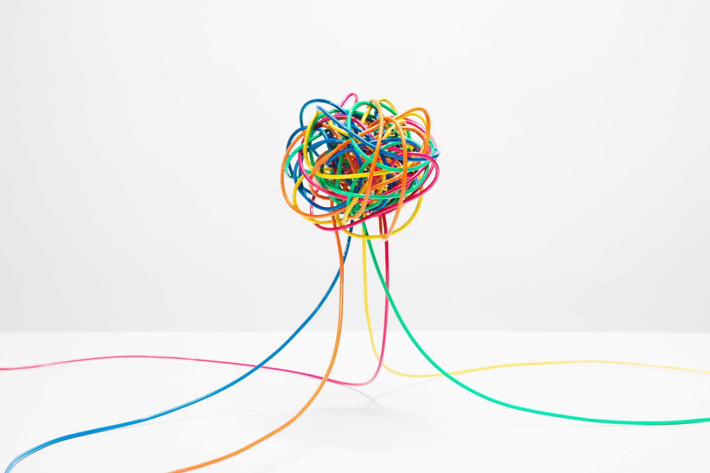 Different colored wires coming together to create a ball in mid air on white background