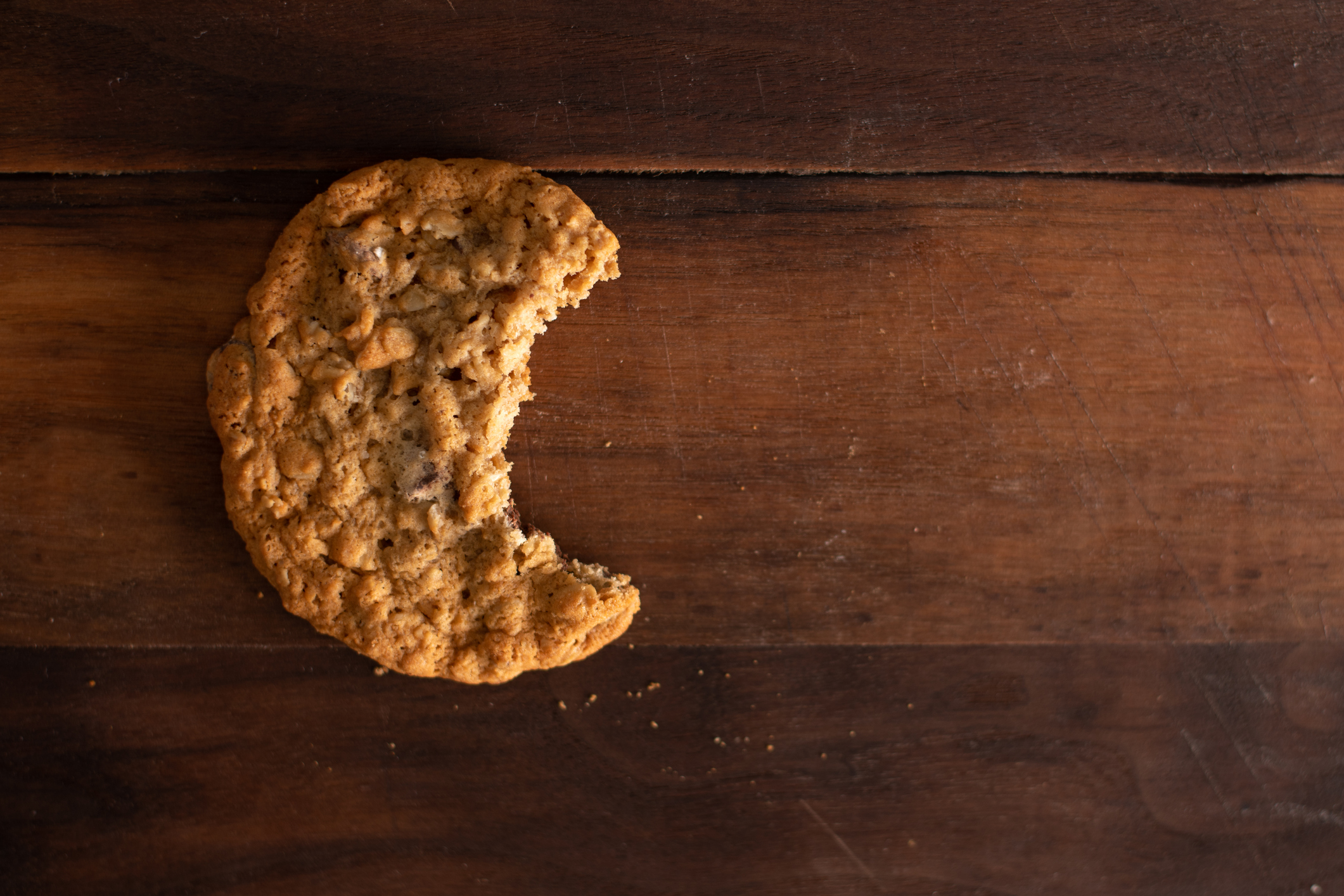An oatmeal chocolate chip cookie with a bite out of it on a walnut wood board.