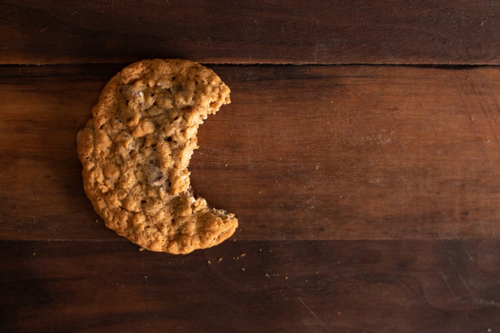 An oatmeal chocolate chip cookie with a bite out of it on a walnut wood board.