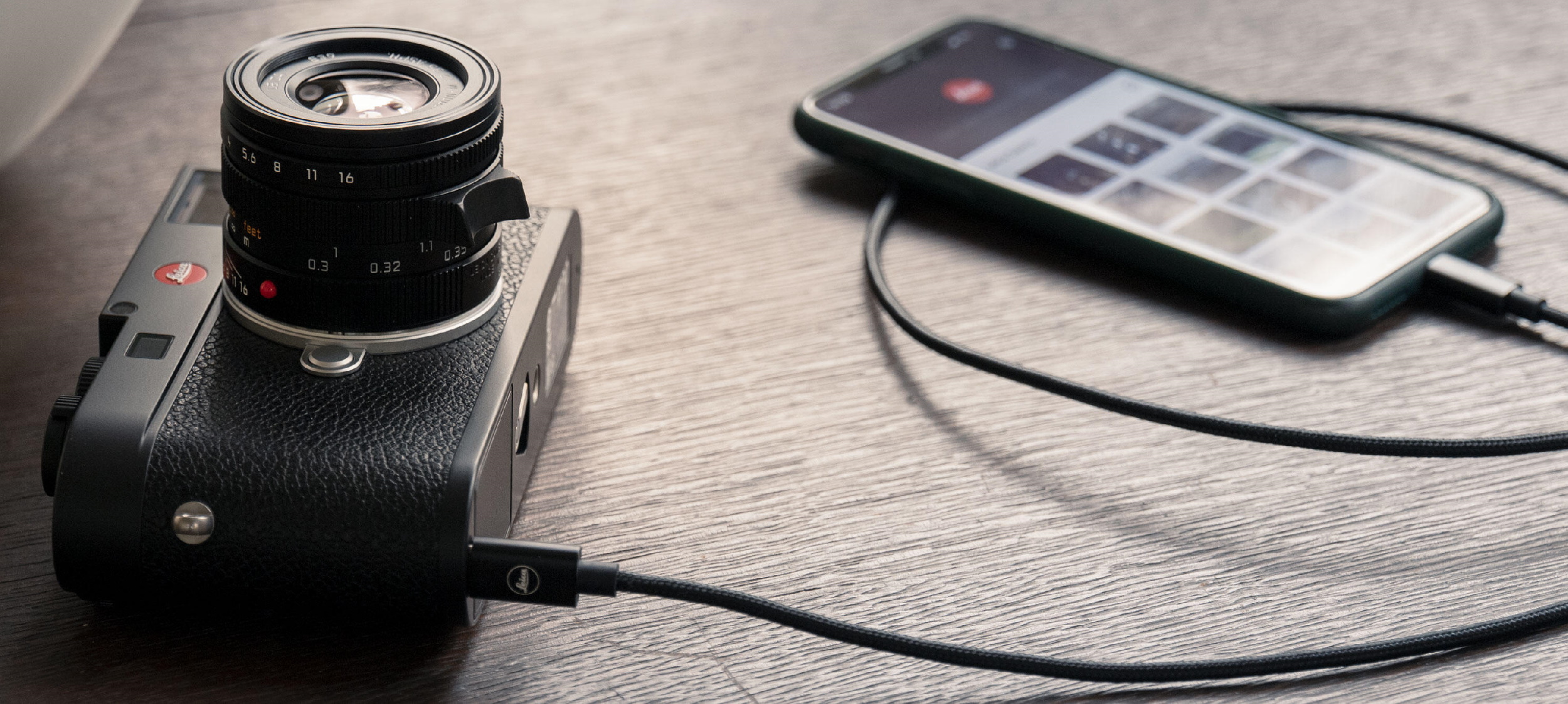 A Leica M11 on a table plugged into a phone.