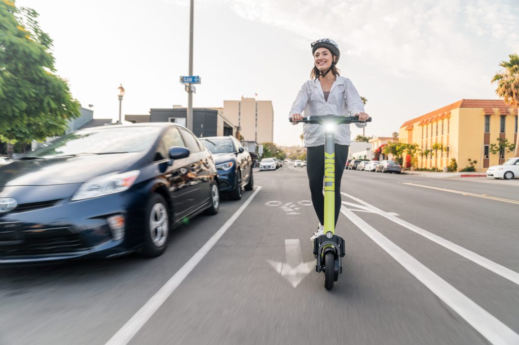 Smiling woman rides LINK superpedestrian e-scooter in bike lane