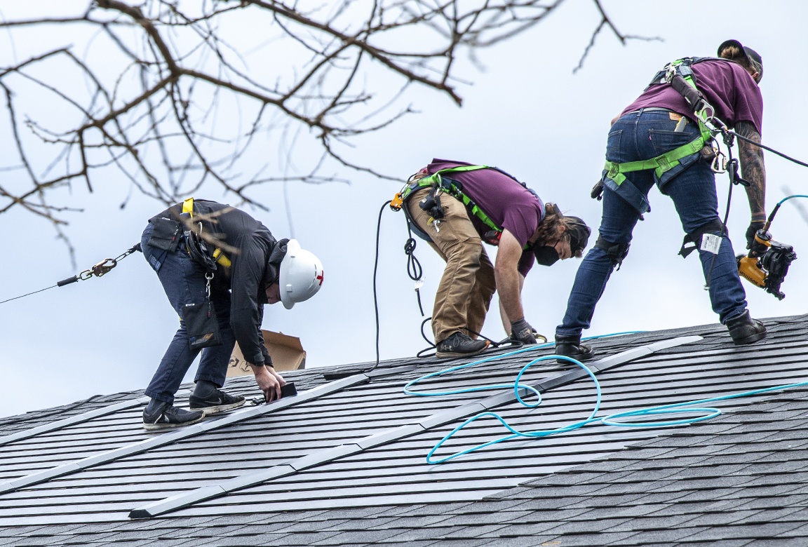 Roofers install a solar shingle on a roof.