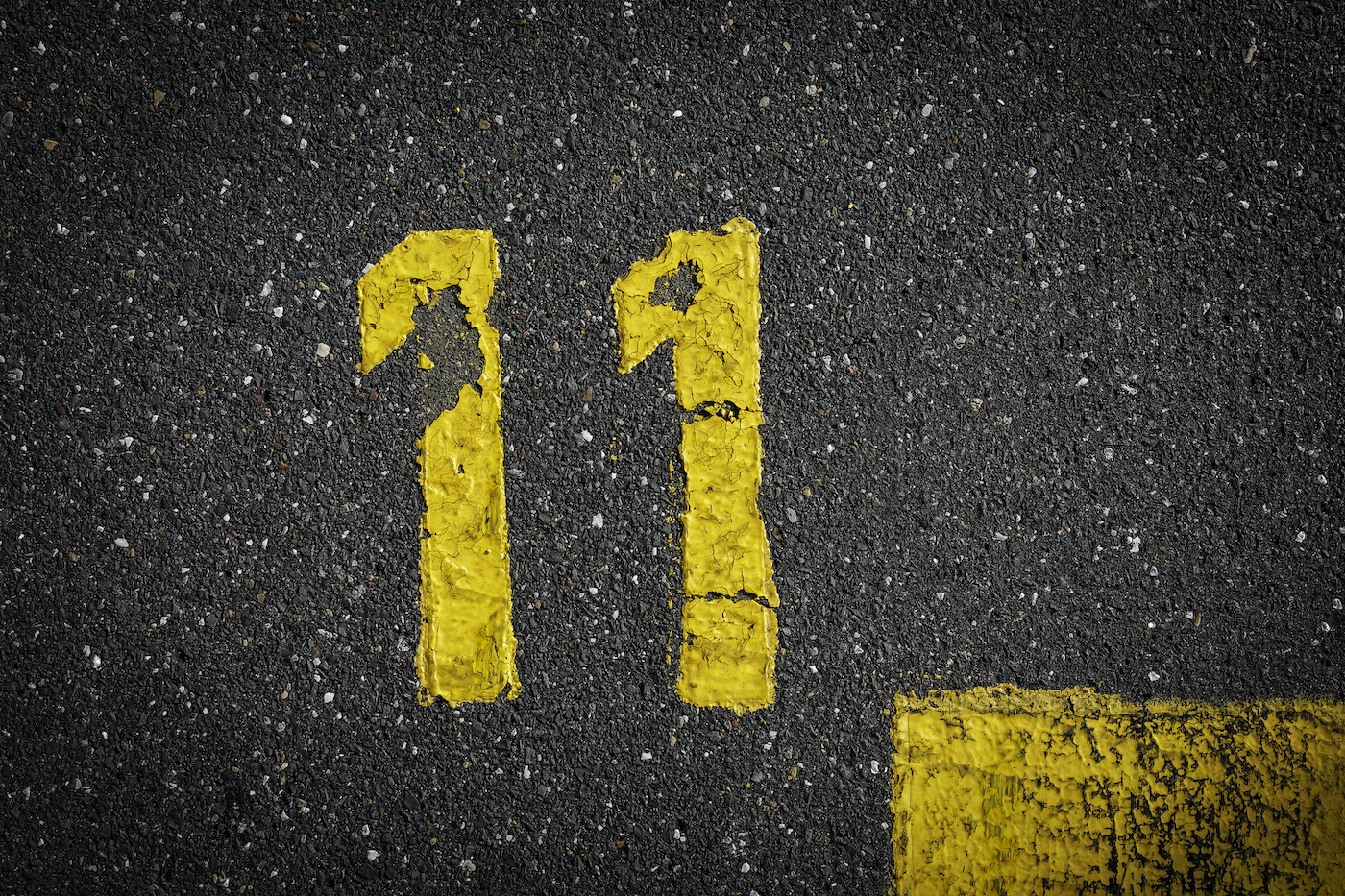 skilt på asfalten, gulmalet nummer elleve på grå gade, gule streger som et hjørne på vejen, plads til tekst