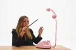 Image of a young businesswoman pointing magicians wand at levitating telephone receiver.