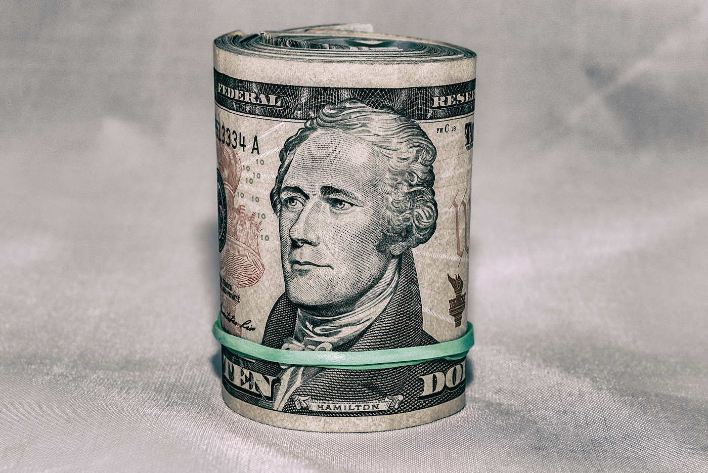 A roll of US currency with a $10 bill on the outside, Alexander Hamilton's portrait in the center.