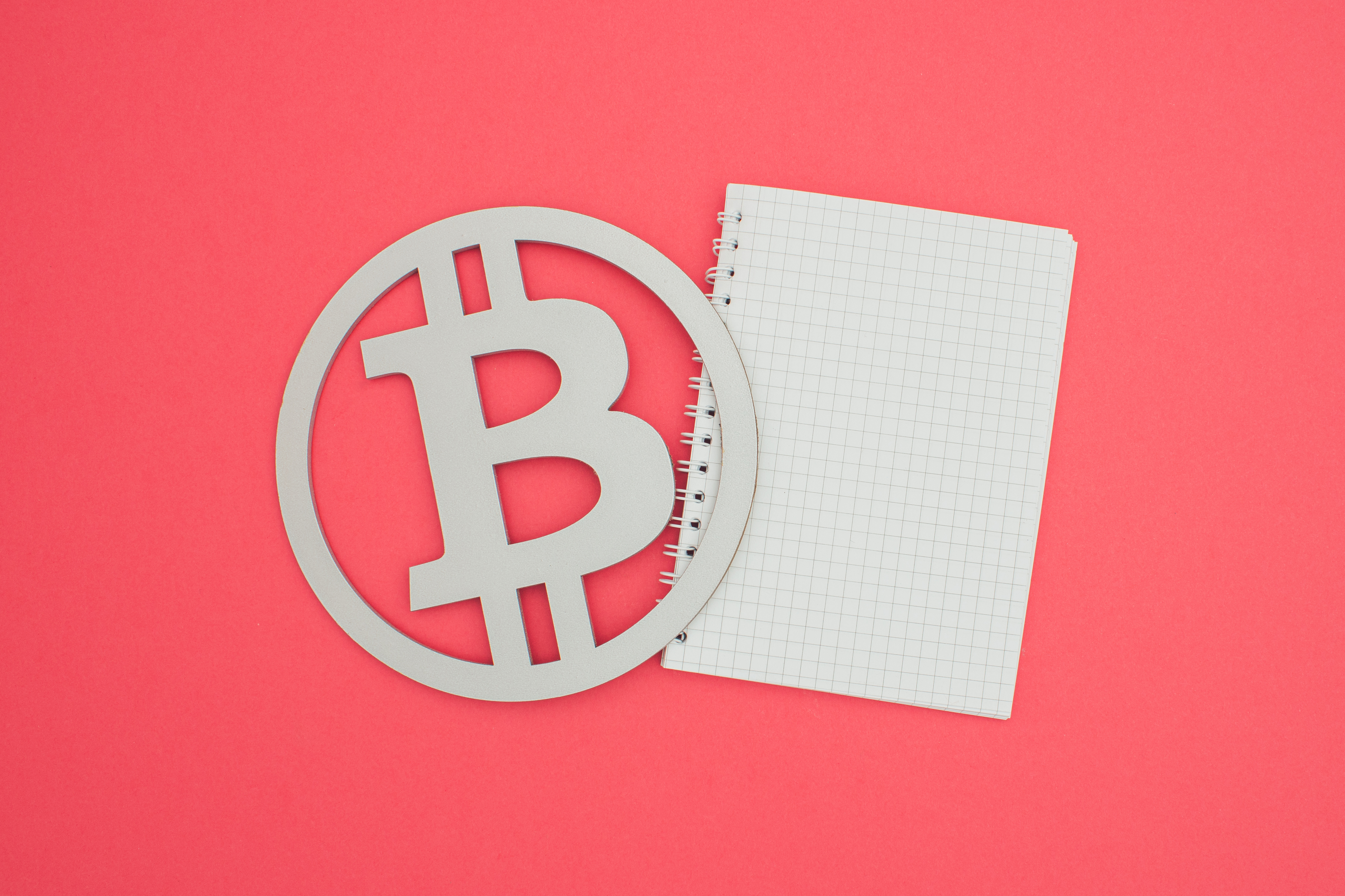 Bild des Bitcoin-Symbols und des weißen Notizbuchs auf lachsfarbenem Hintergrund.