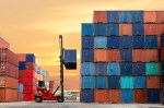 forklift hoisting a shipping container onto stack of containers
