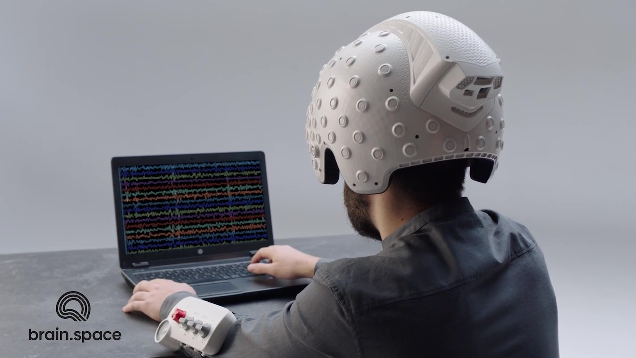 A person holding a brain.space headset working on a computer.