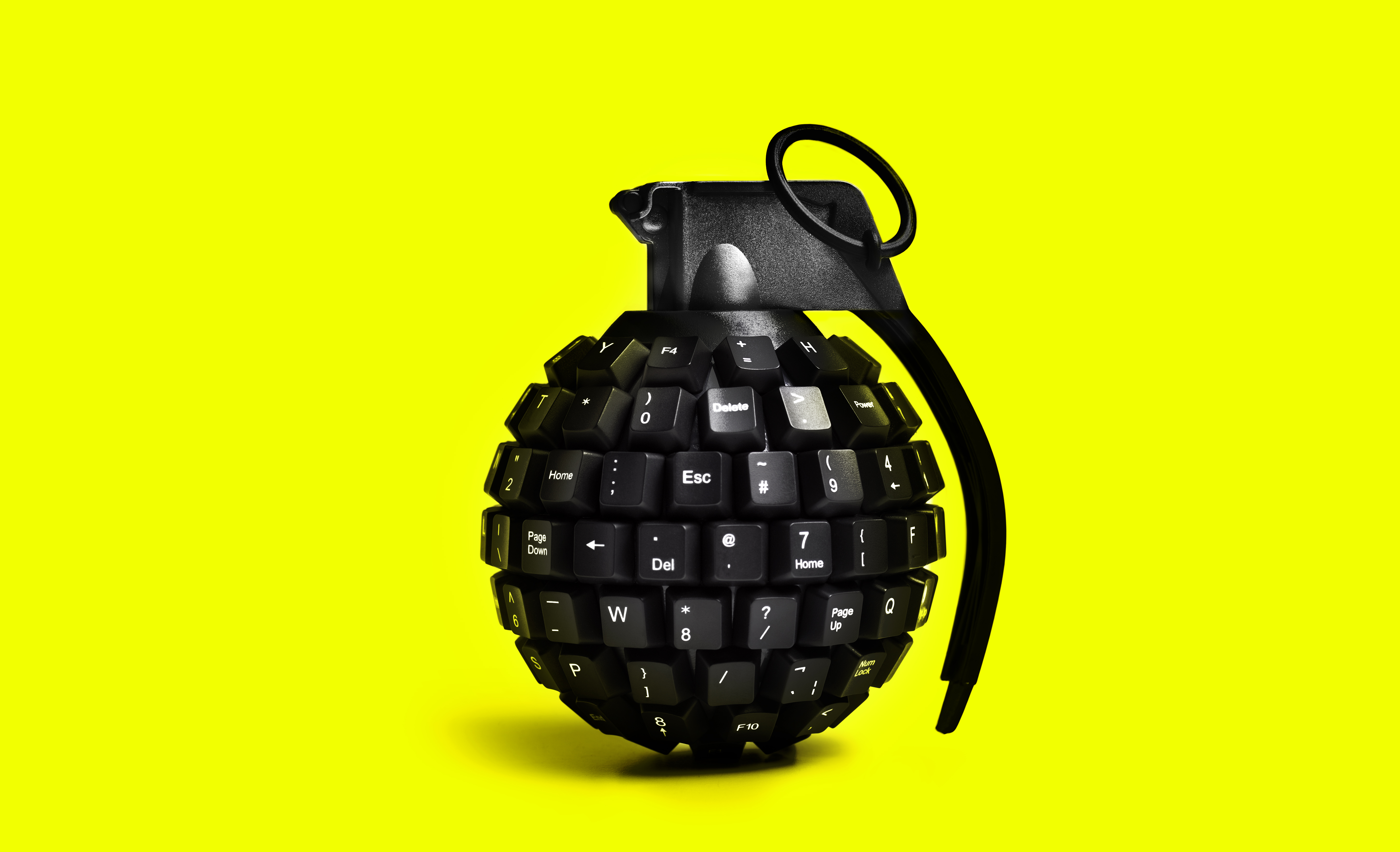 Image of a grenade made from computer keys against a neon yellow background.