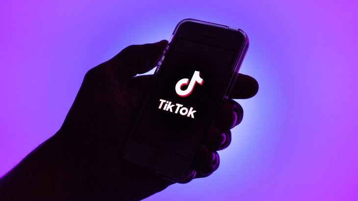 TikTok logo illustrated on mobile phone held in a hand