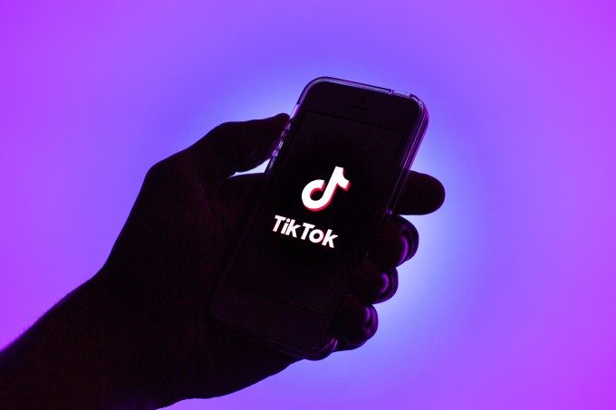 Tiktok logo on a handheld phone in silhouette with a purple background