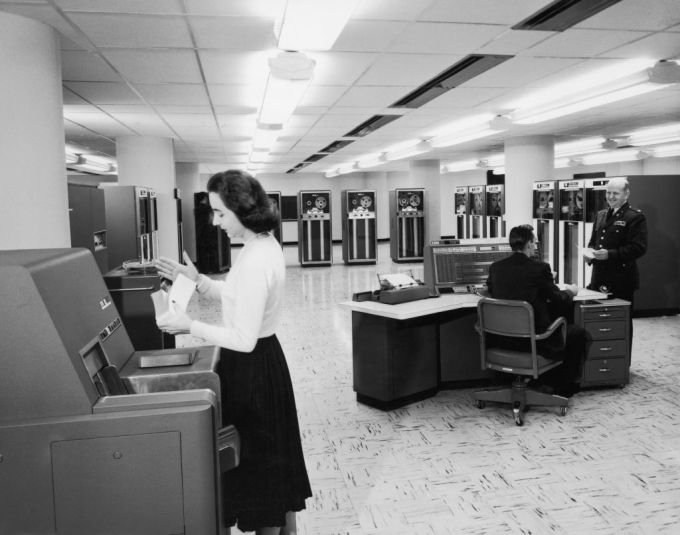 Sala de ordenadores de los años 50 con mainframe y máquina de tarjetas perforadas.