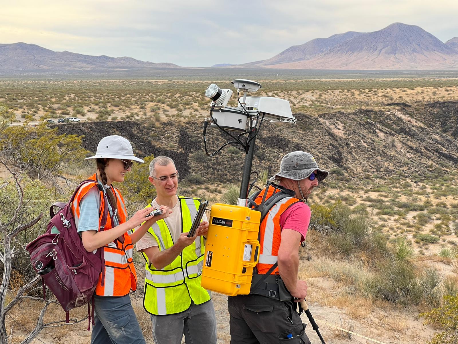 Researchers attach a lidar unit to another's back in the desert.