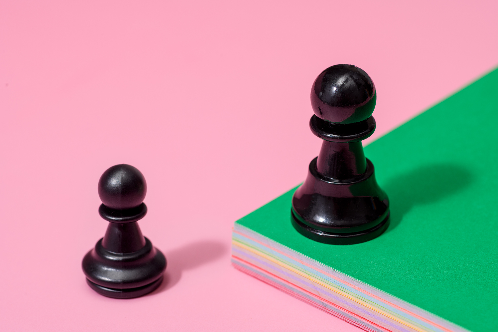 одна шахматная пешка на зеленой приподнятой платформе и одна на нижней розовой платформе.  стартапы и рыночные спады
