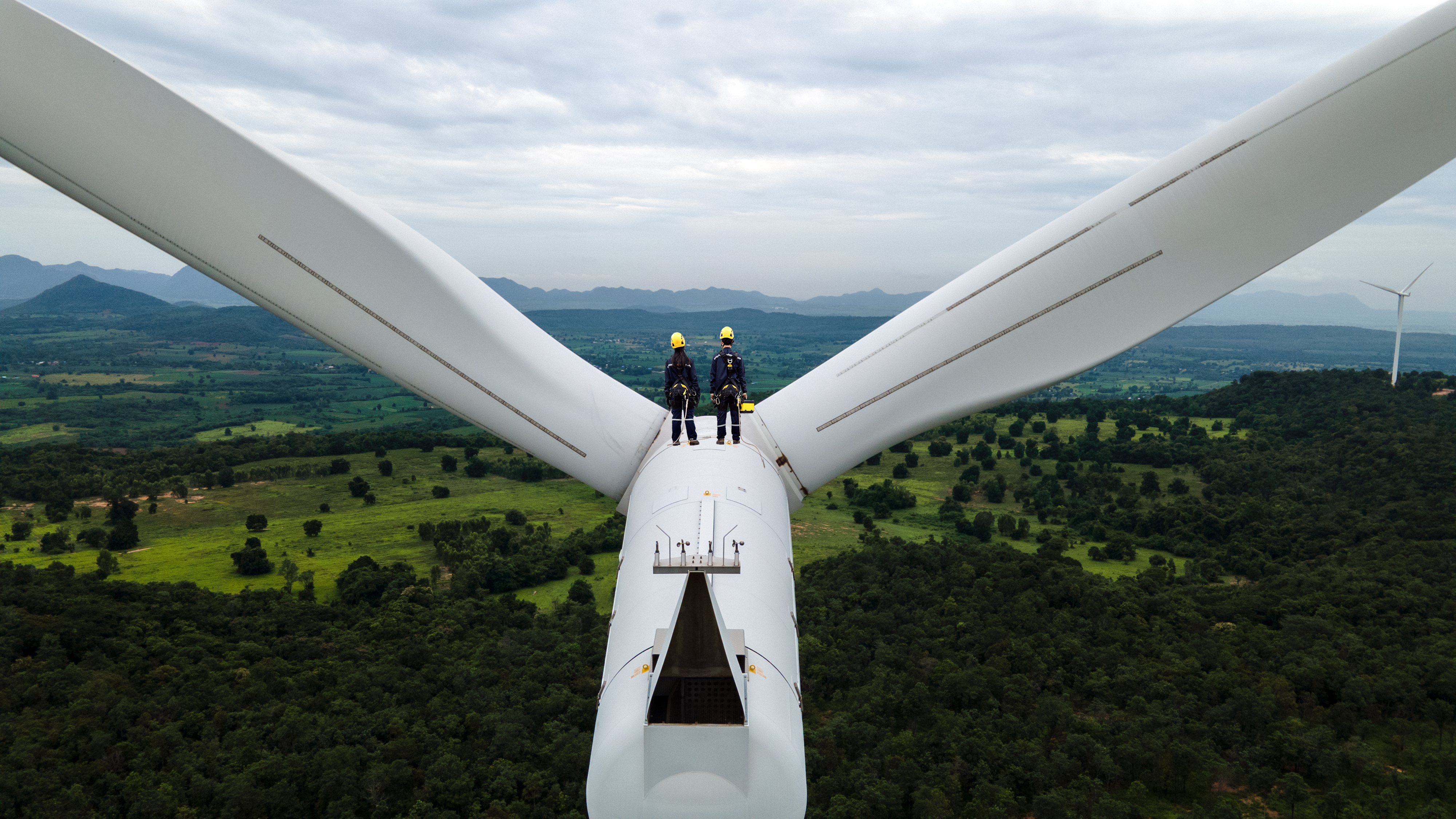 Dos ingenieros eléctricos que usan equipo de protección personal trabajando en la parte superior de la granja de turbinas eólicas;  encuesta de inversionistas en tecnología climática