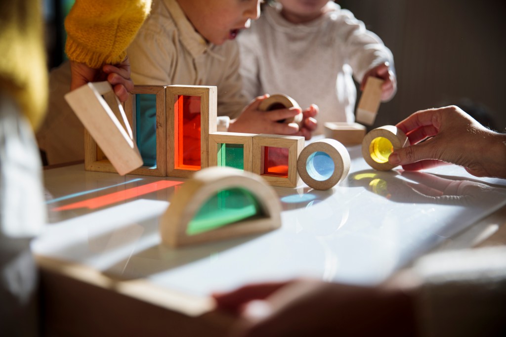 Little kids playing with colorful wooden building blocks on the table, used in a post about childcare startup Kinside