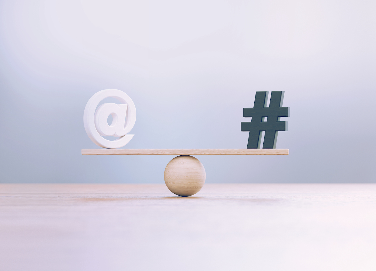 White at and black hashtag symbols sitting over wooden seesaw scale before defocused background.