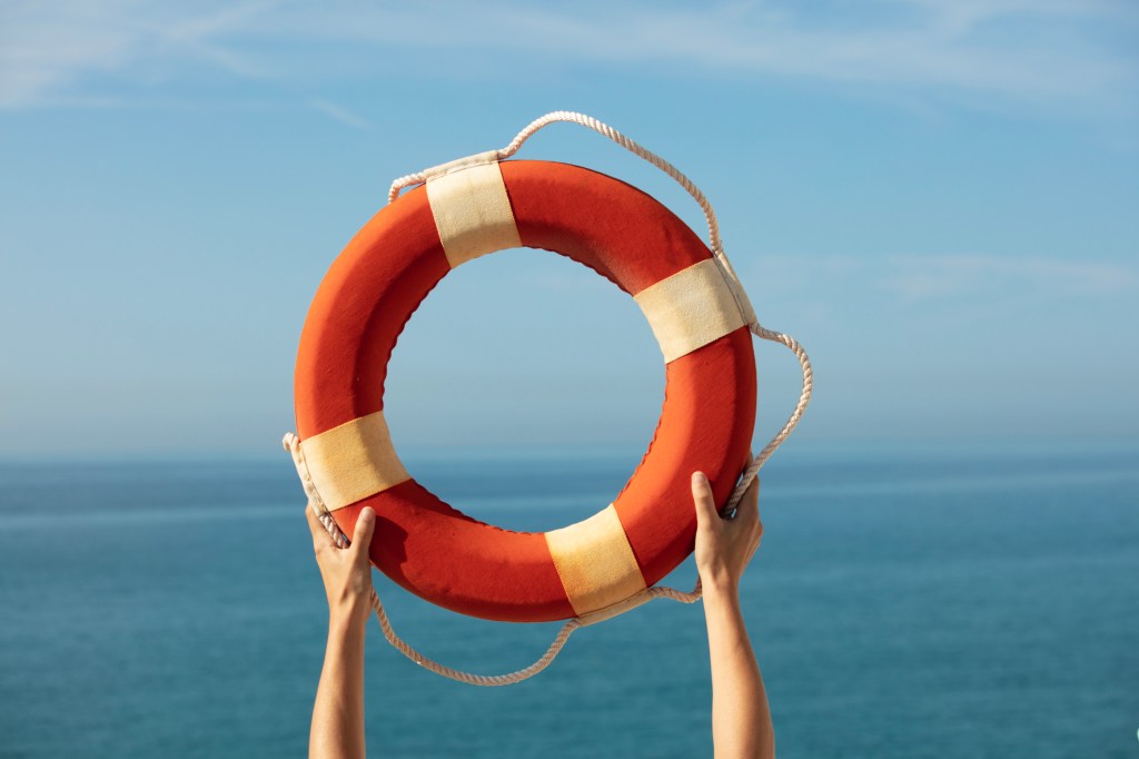person holding lifeguard ring/float in the air, facing water