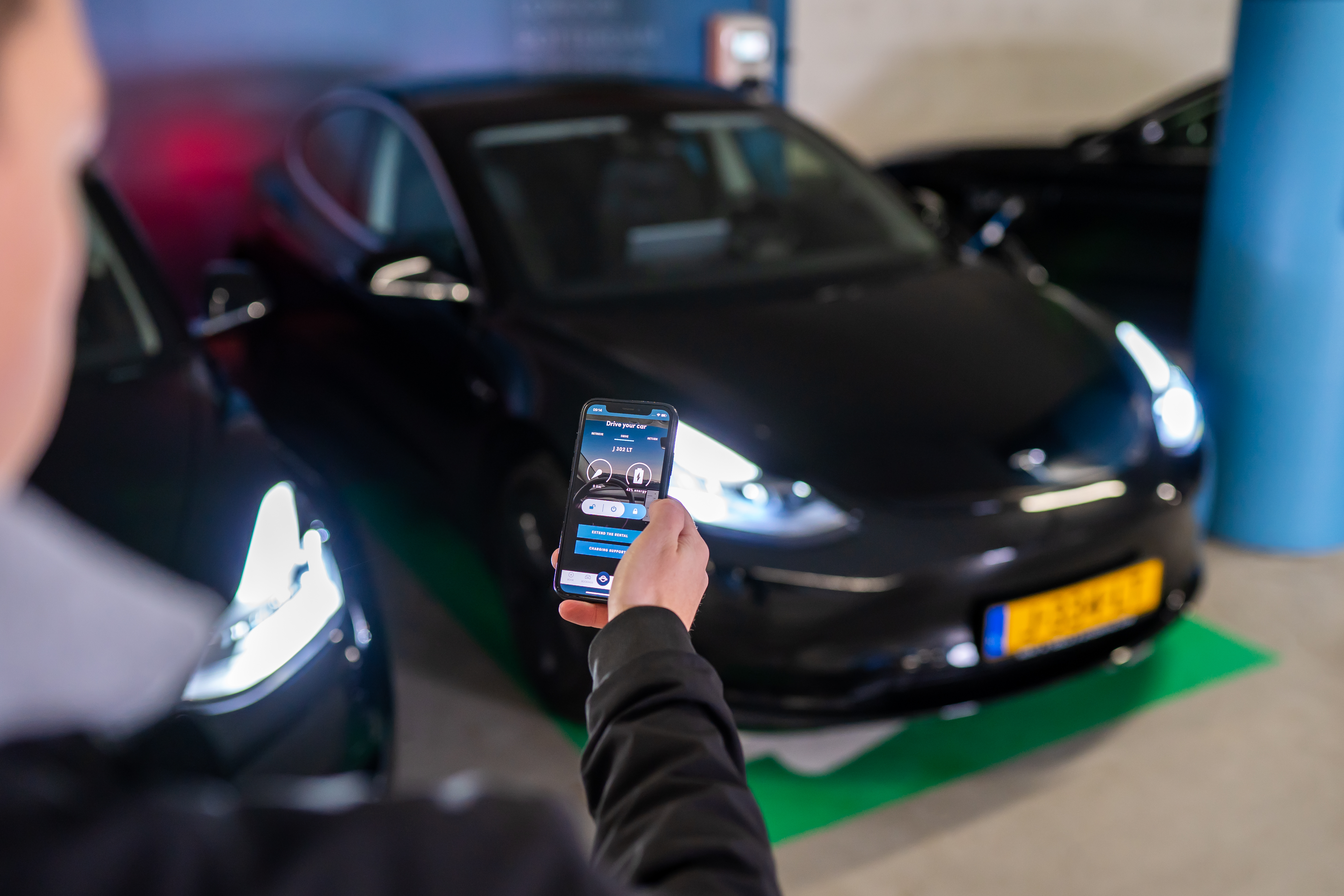 a man holds up his phone to unlock a rented tesla via an app