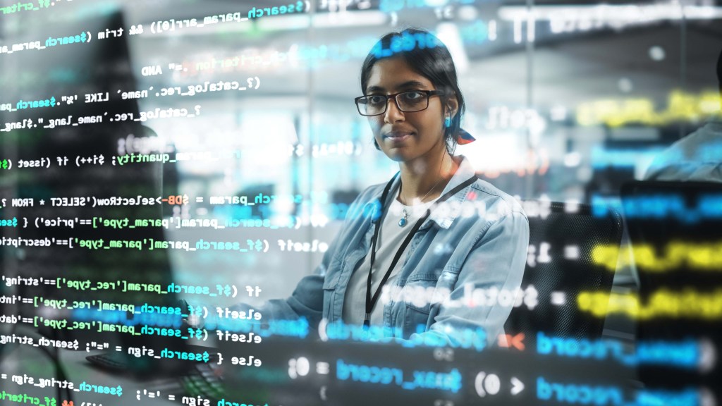 Diverse Office: Portrait of Confident Indian IT Programmer Working on Desktop Computer. Professional Female Specialist Develop Innovative Software. Shot with Visual Effects of Running Code.