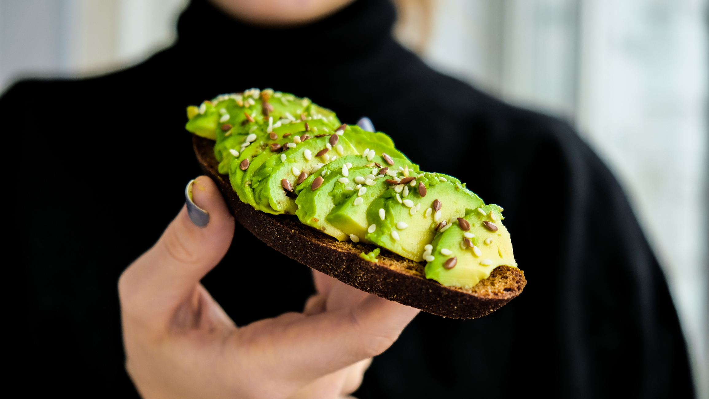 Hand-held avocado toast.  Ripe Hass Avocado, Whole Grain Bread, Sesame Flax Seeds.