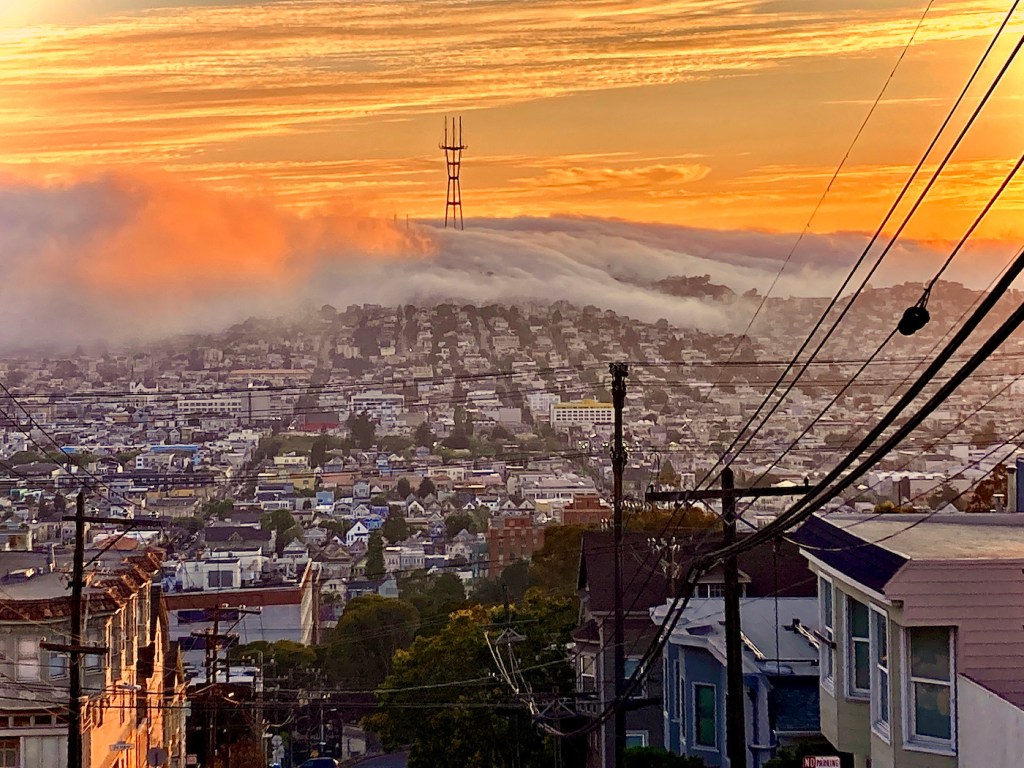 San Francisco brilliant sunset with fog rolling over Twin Peaks and Sutro Tower and clouds in sky.