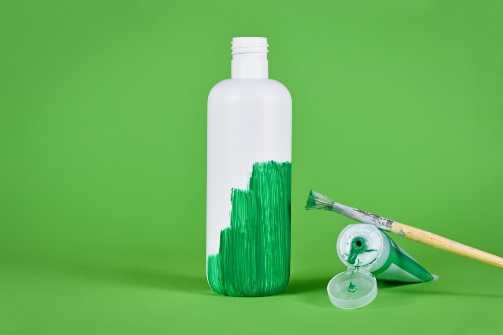 White plastic bottle being painted green; greenwashing