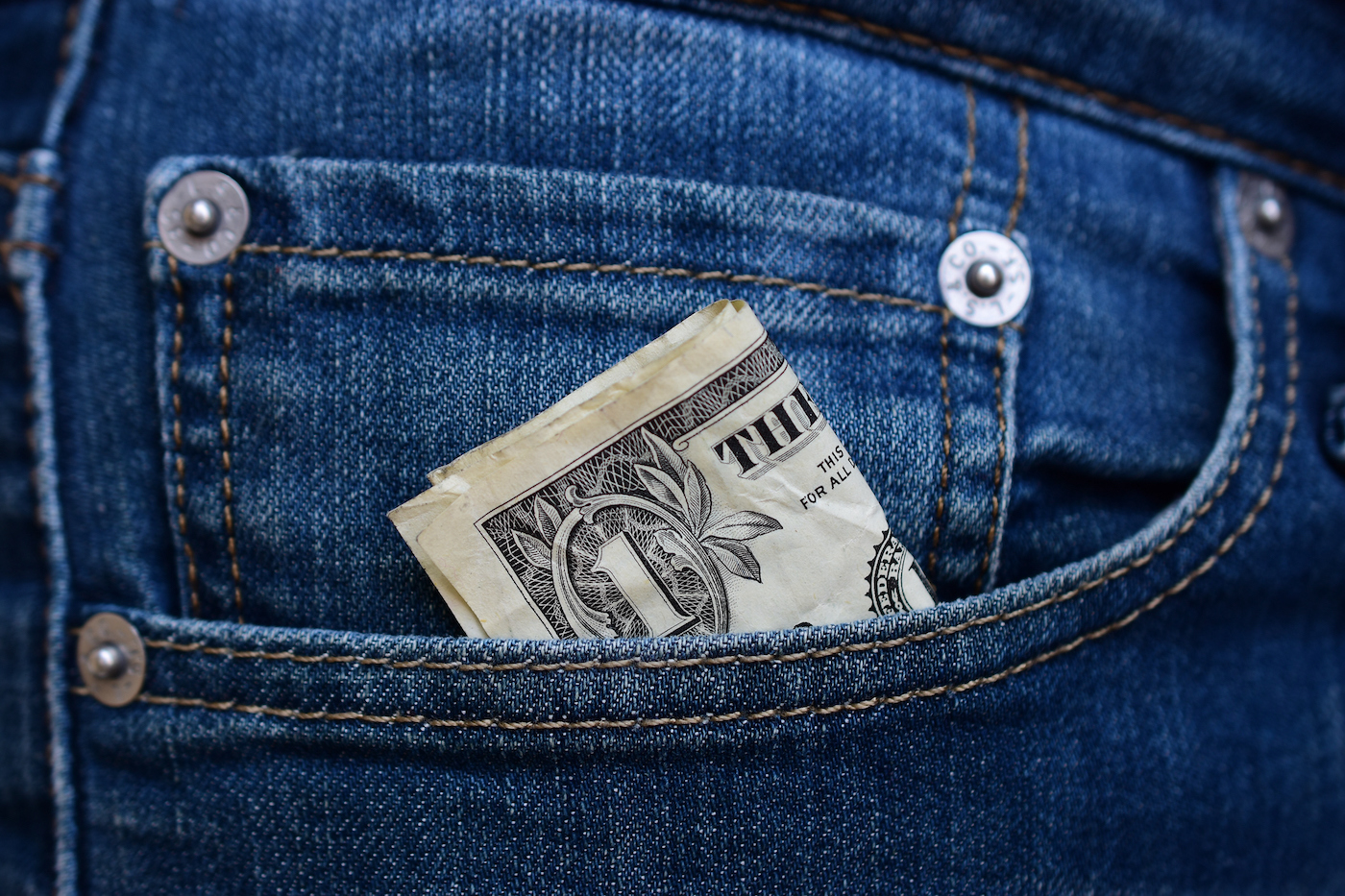 A folded dollar bill slips into the front pocket of a pair of jeans.