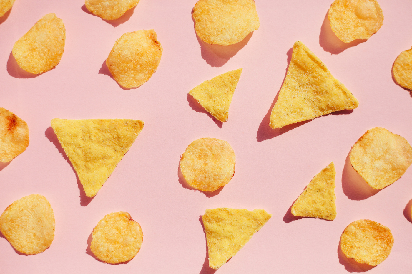 Padrão de batatas fritas sobre fundo rosa, luz dura com sombras.  Conceito de junk food insalubre.