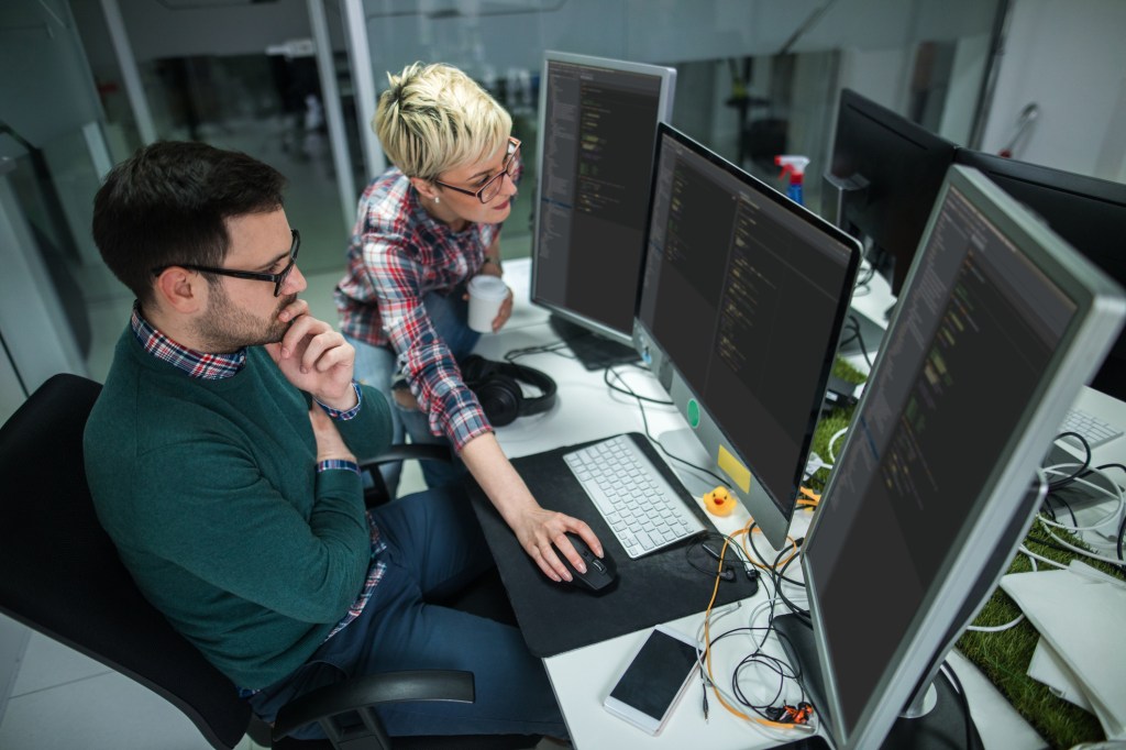 Two software developers at work in front of three computer monitors, used in a post about TestGrid