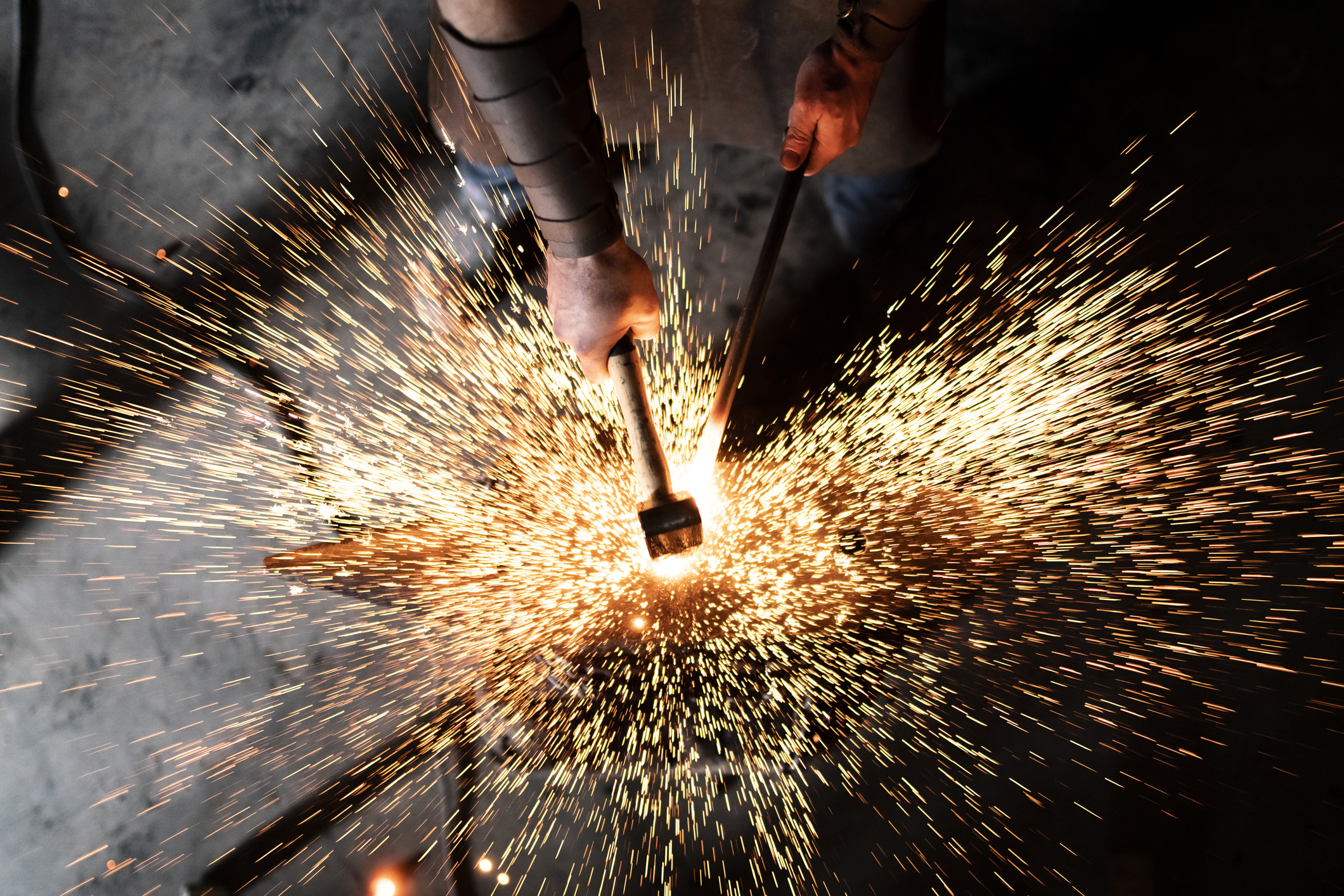 Seorang pandai besi yang terampil bekerja di bengkelnya dengan palu besi bersuhu tinggi di landasannya untuk membuat karya baru dengan menciptakan banyak percikan api dalam gelap.  Startup perangkat keras
