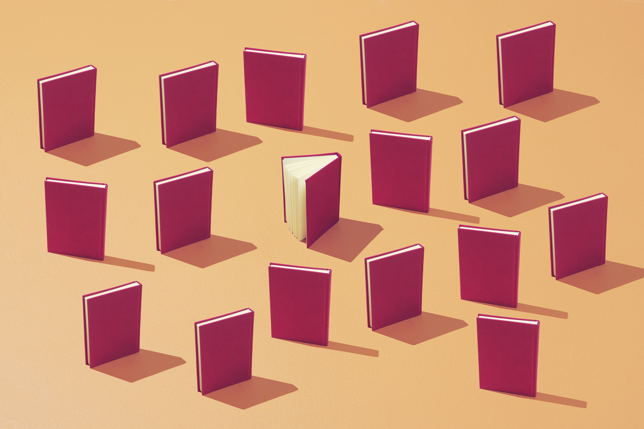 A group of books laid in a pattern on a colorful background. one is standing out from the crowd