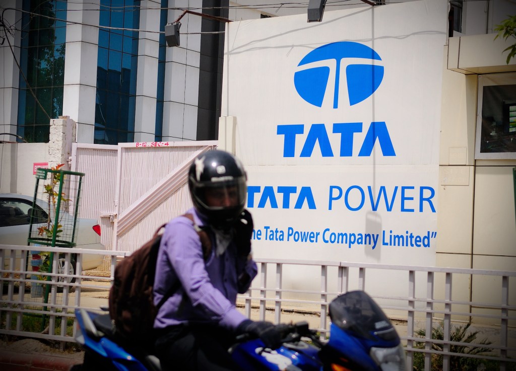 A person on a motorbike speeding past a Tata Power sign on a building in Noida, India