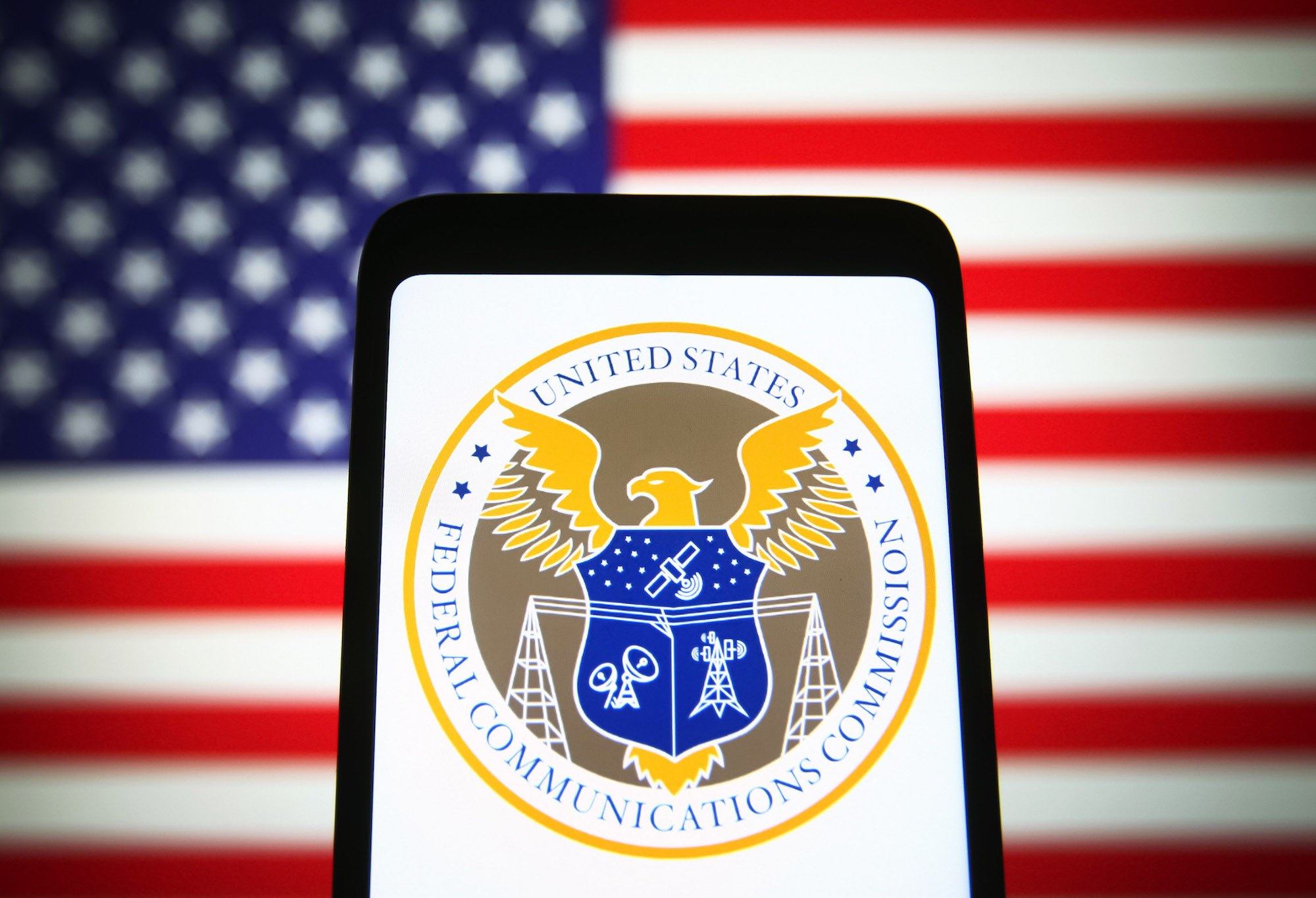 The US Federal Communications Commission (FCC) seal is seen on a smartphone screen with the US flag in the background.