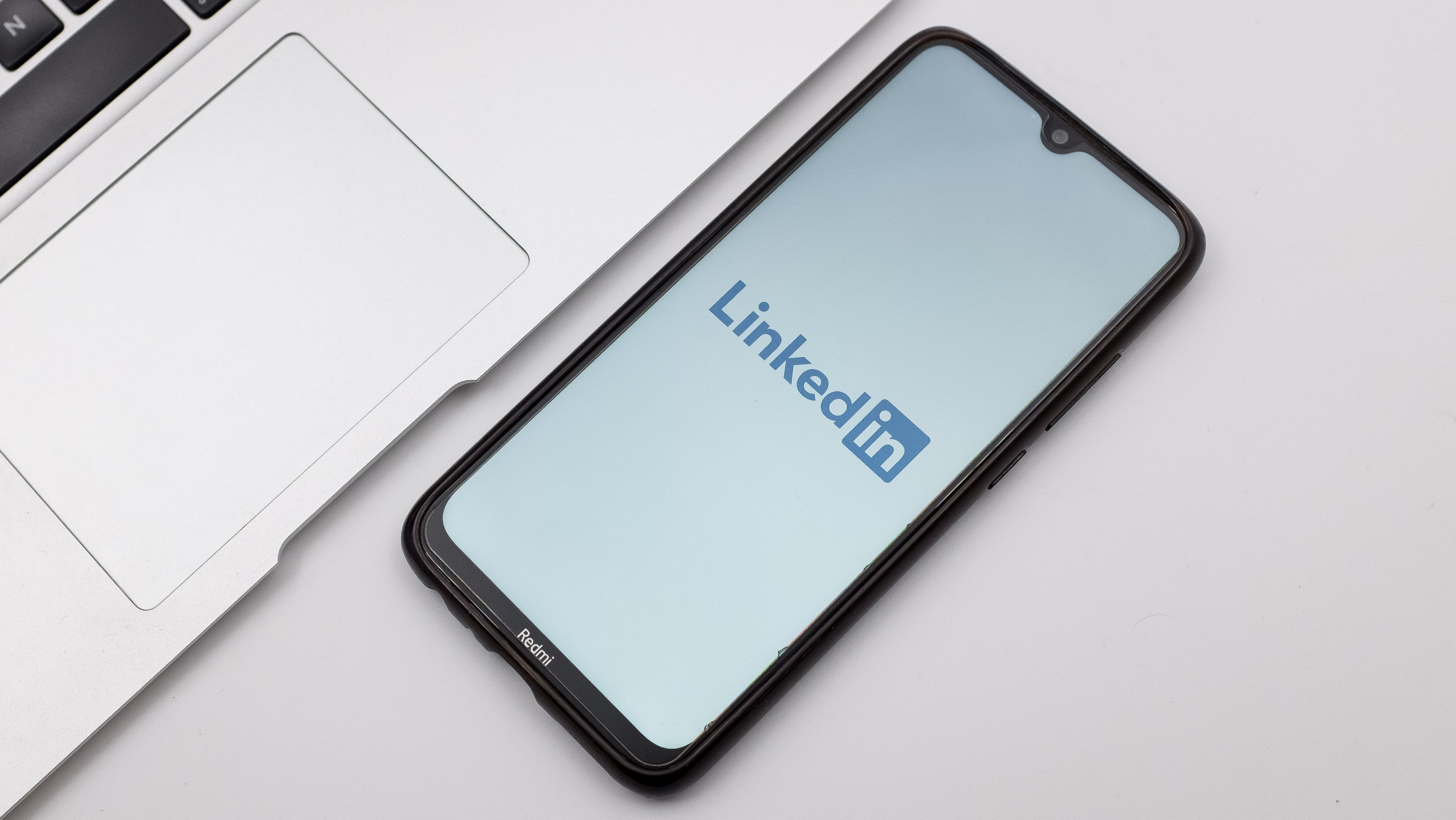 The LinkedIn mobile app is displayed on a smartphone on the desk