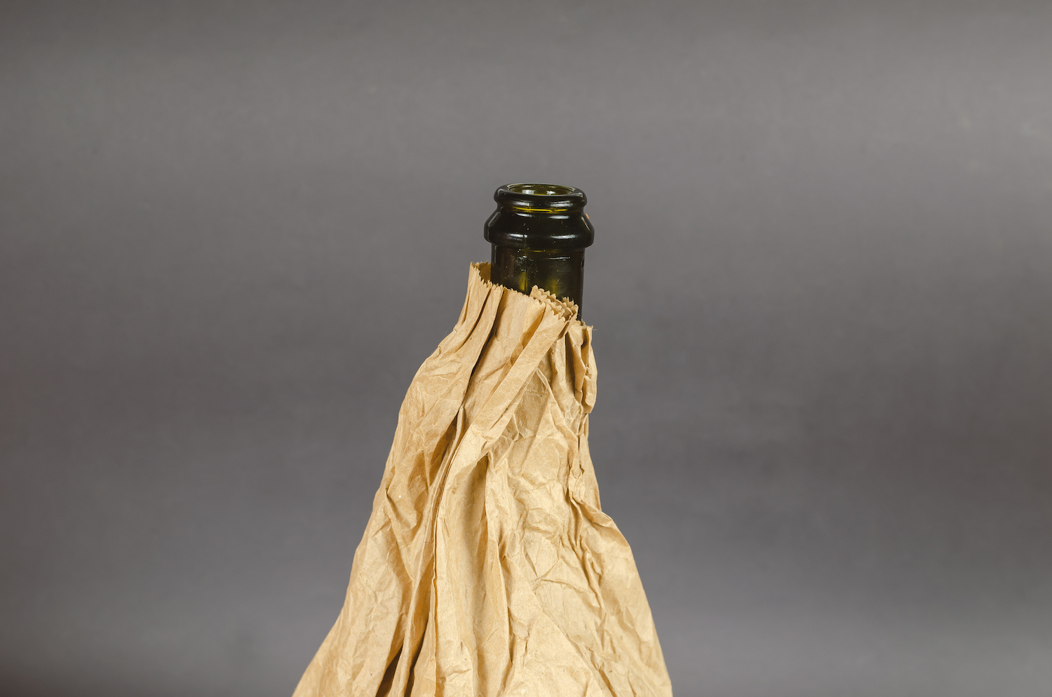Bottle in a paper bag on a gray background. Dark bottle of alcohol in a crumpled brown bag. Close-up. Selective focus.