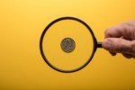 Human hand holding magnifying glass over american quarter on yellow background