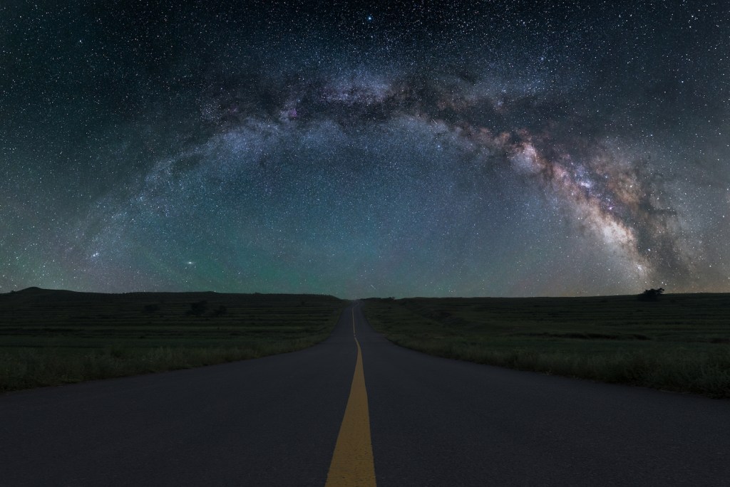 Looking down the center line of a highway at dusk with the Milky Way in the background