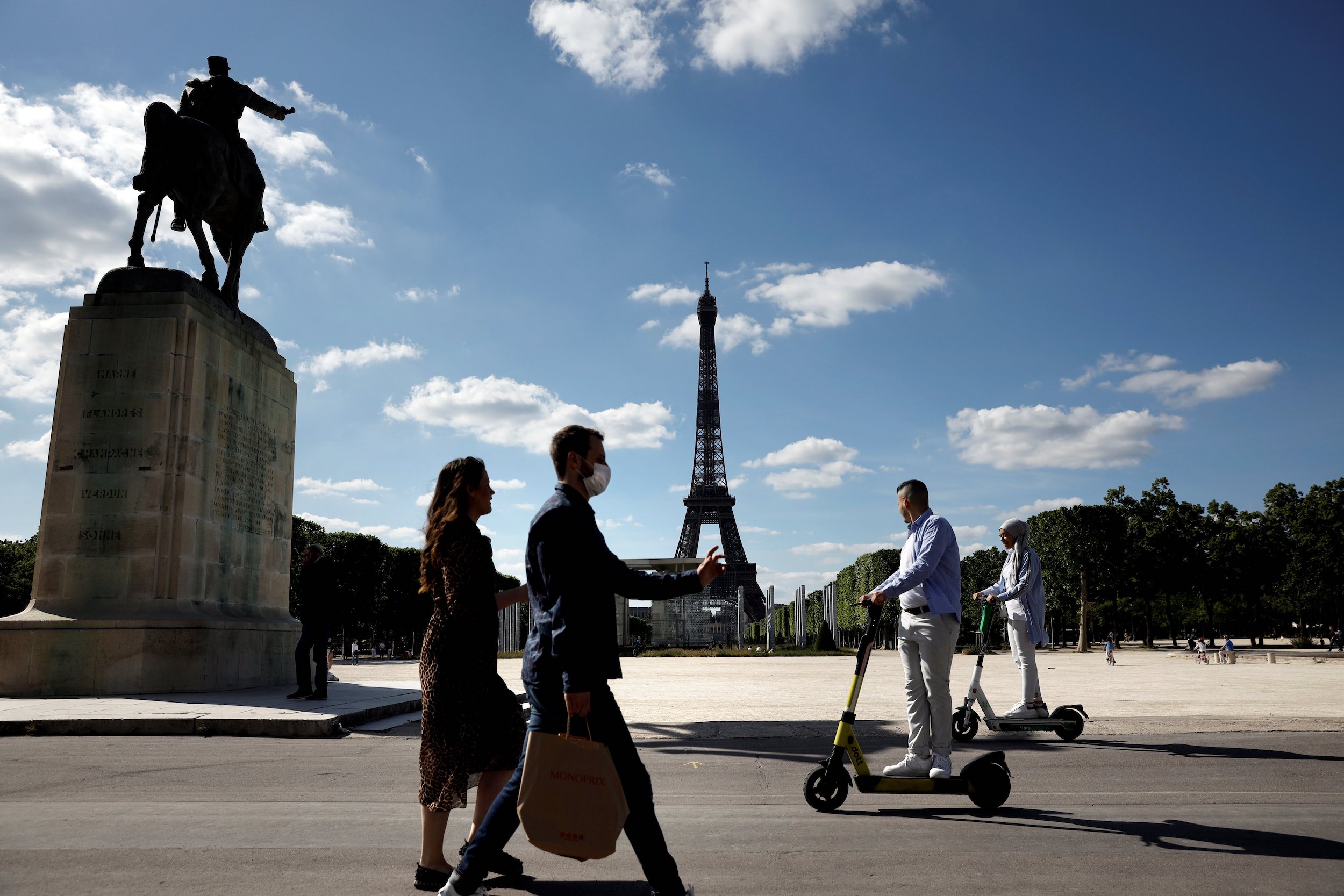프랑스가 COVID-19의 확산을 억제하기 위해 취한 봉쇄 조치를 완화함에 따라 2020년 5월 19일 파리에서 배경에 에펠탑이 있는 Marechal Joffre의 동상을 지나서 보호용 안면 마스크를 착용한 사람들이 걷거나 전기 스쿠터를 타고 있습니다. (신종 코로나바이러스). 