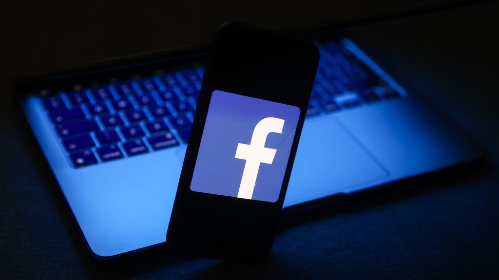 Facebook logo displayed on a phone screen and a laptop are seen in this illustration photo