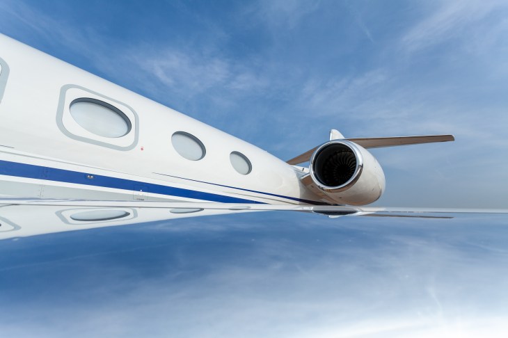 A Gulfstream G650 private jet. Wide angle view of the fuselage, wing and engine with blue sky reflections.