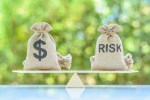 Photo of money bag balanced with bag labeled with "risk" on a scale