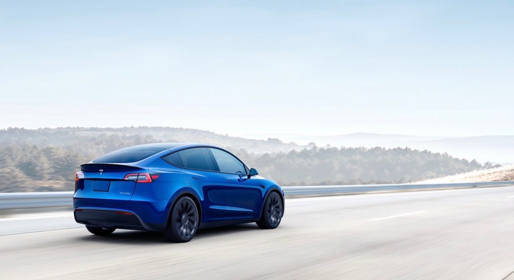 A blue Tesla Model Y drives on a road