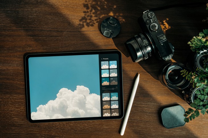 Directly above shot of digital tablet, camera and lens on rustic wooden desk against sunlight. Designer / photographer's collection on workstation