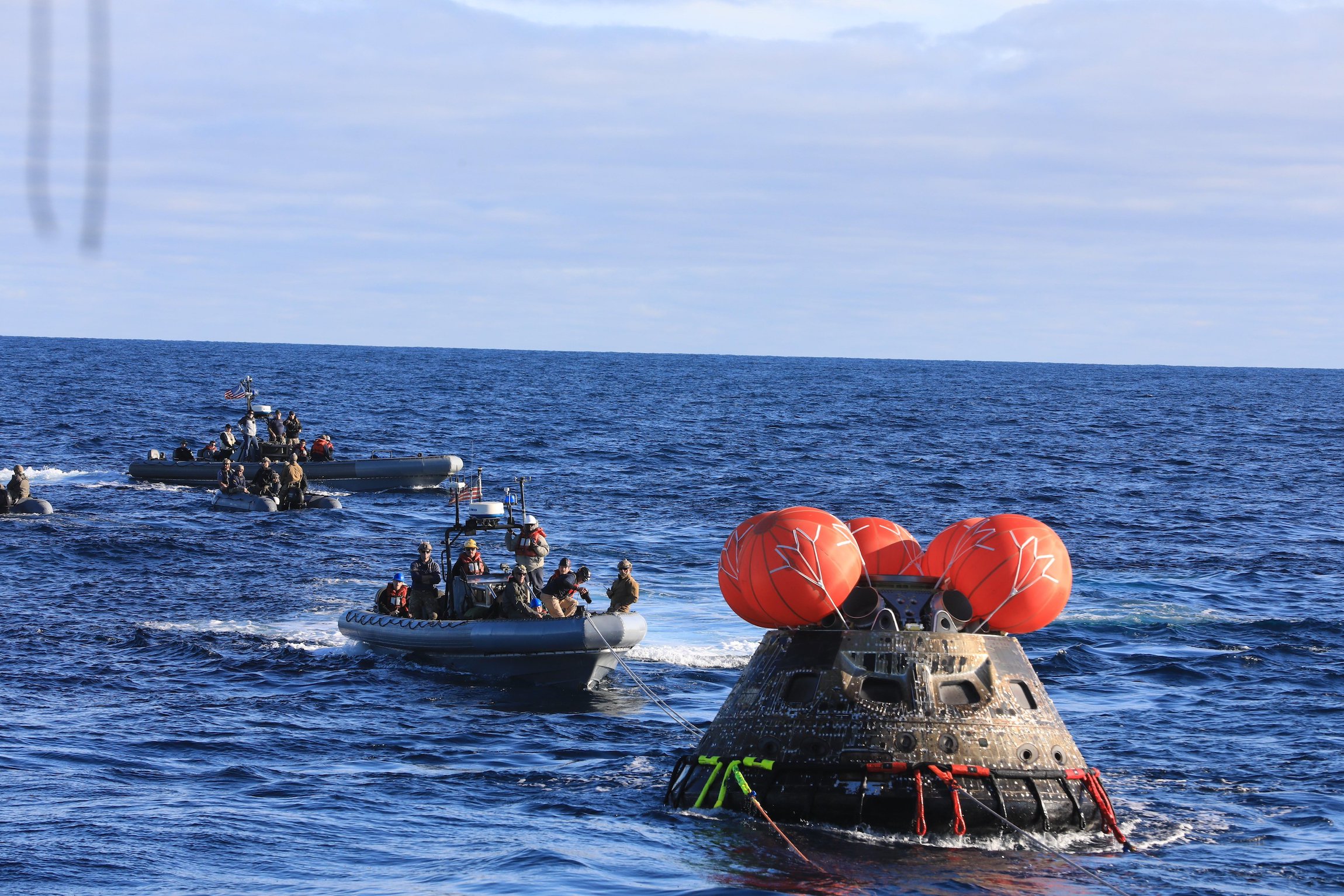 Orion space capsule after splashdown in the Pacific Ocean; crews approaching in recovery boats