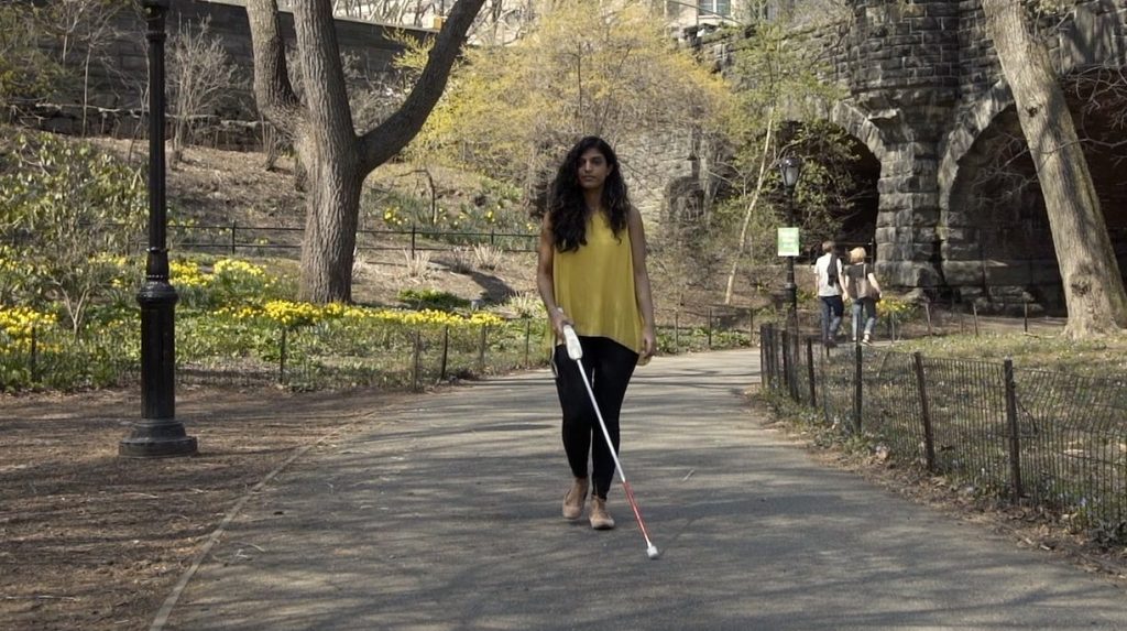 Woman walking on a path in a park using a WeWalk Smart Cane