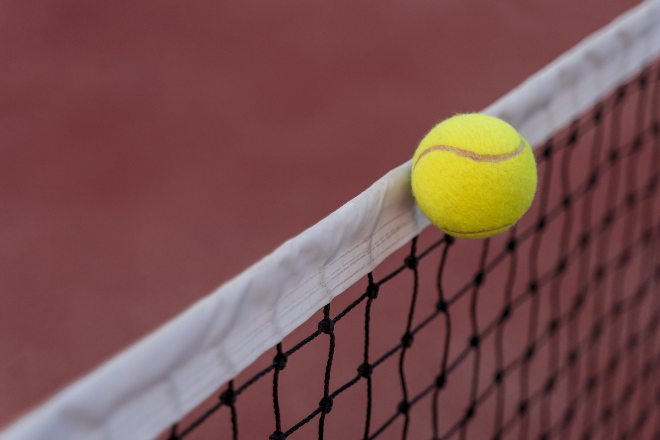 A tennis ball hitting the net on a red field.